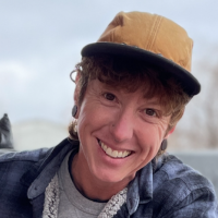 A smiling person wearing a tan cap and plaid shirt outdoors. A smiling person wearing a tan cap and plaid shirt outdoors.